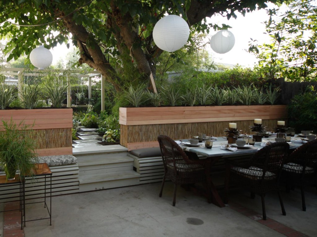 This gorgeous outdoor dining area is accented by white Chinese lanterns, comfy bench seating, plenty of shade, a gorgeous stone walkway and a mid-rise flower bed filled with ornamental grasses. Design by Jamie Durie